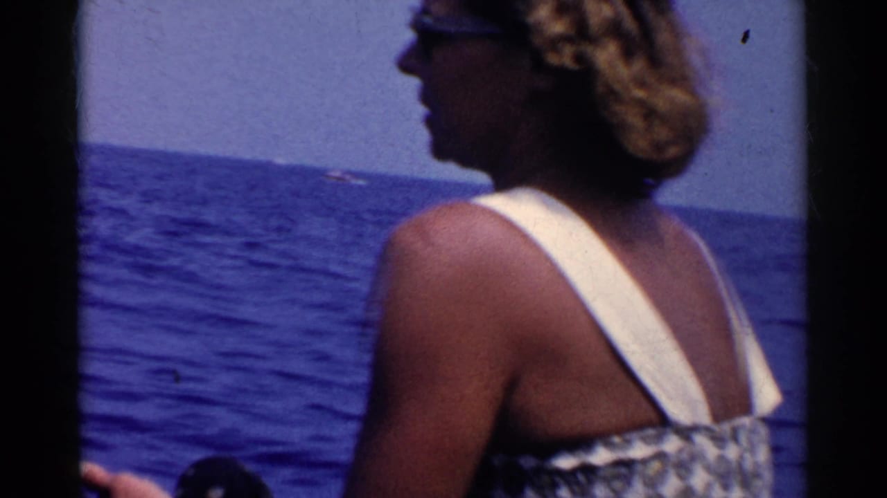 Woman in sunglasses stands on a boat beside the blue ocean.