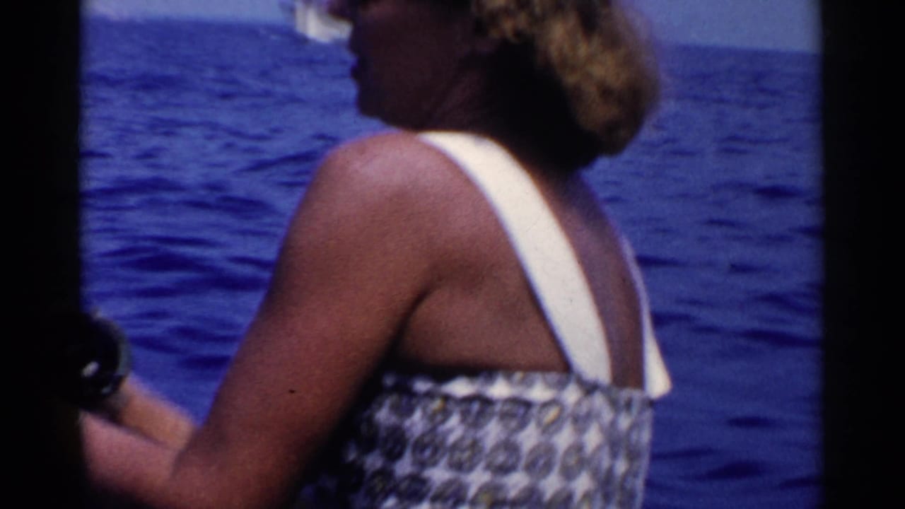 In 1955 California home-movie footage, a woman in sunglasses and a patterned swimsuit fishes from a boat on open blue water.