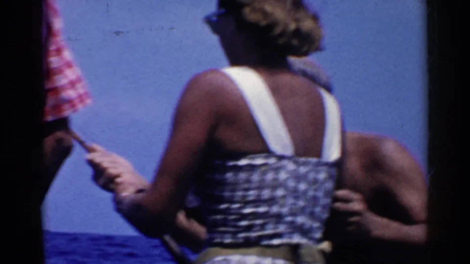 A woman in a sleeveless patterned dress is seen from behind holding a fishing rod on a California boat in 1955 footage.