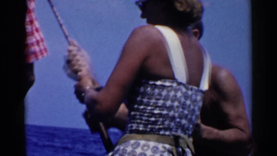 The 1955 California 8mm frame shows a woman lifting or steadying a fishing rod during a sunny boat outing.