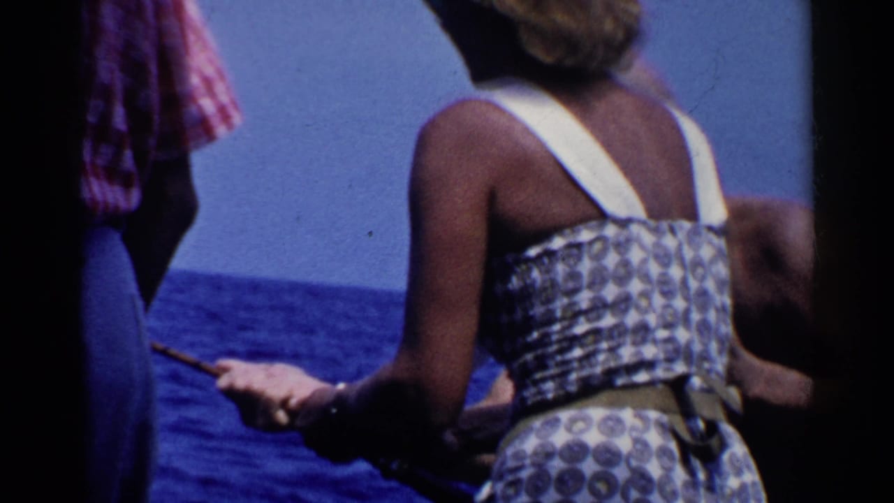 Woman in patterned summer dress on a boat beside a man in a red plaid shirt, with open ocean behind them.