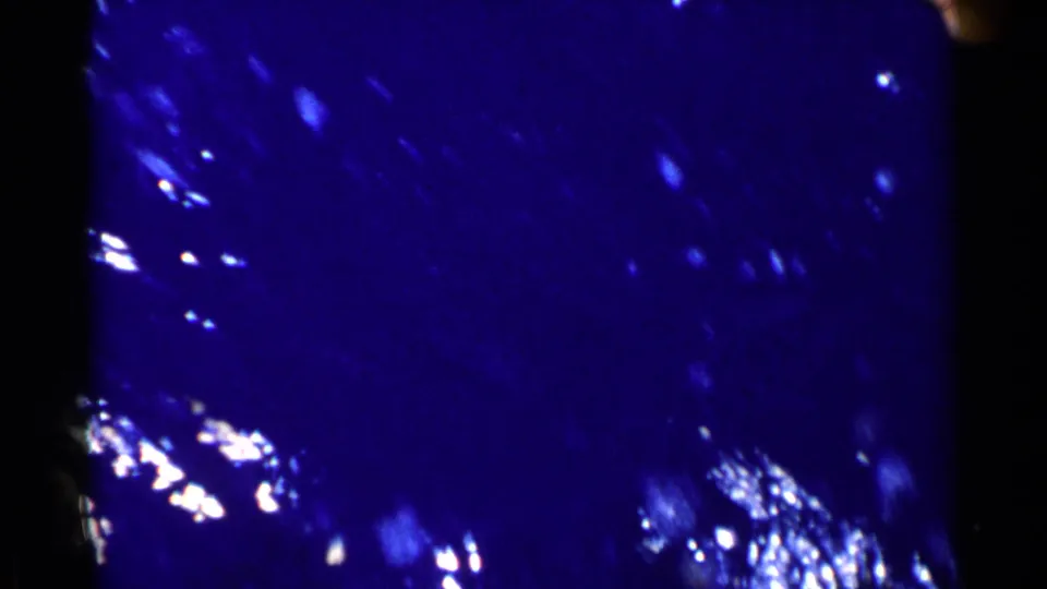 1955 California 8mm frame showing dark blue underwater texture with scattered white highlights, mottled shapes, and strong grain across the lower portion.