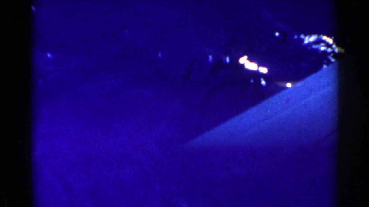 Dark blue underwater or water-surface view with bright reflections and heavy film grain.