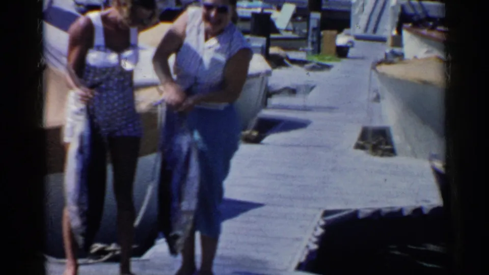 On a sunlit California dock, two women stand close together while one adjusts or holds a large tuna fish for the camera.