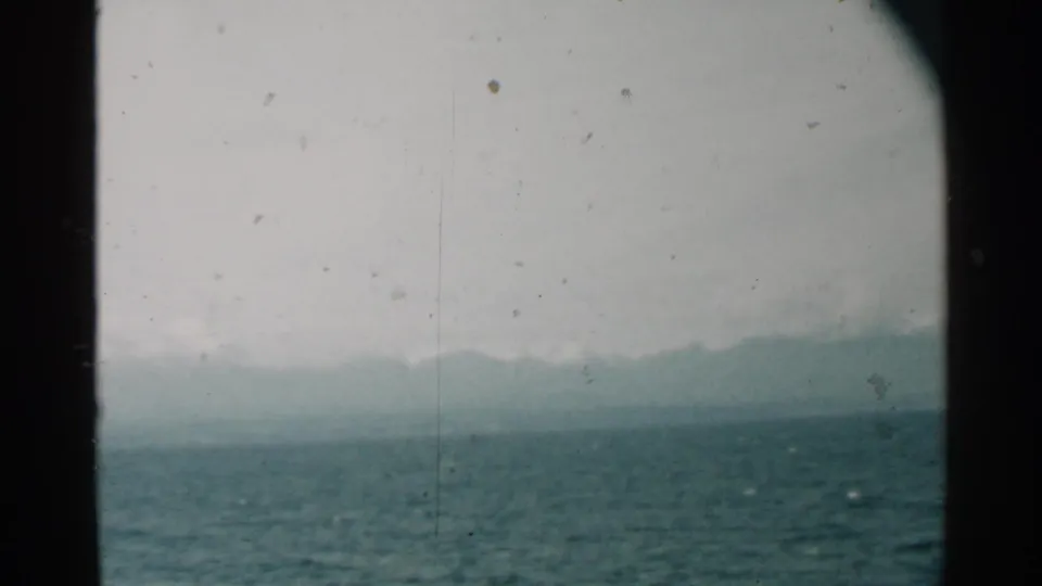 1958 Pearl Harbor home-movie frame showing blue-green water, a faint mountain horizon, and dark porthole edges.