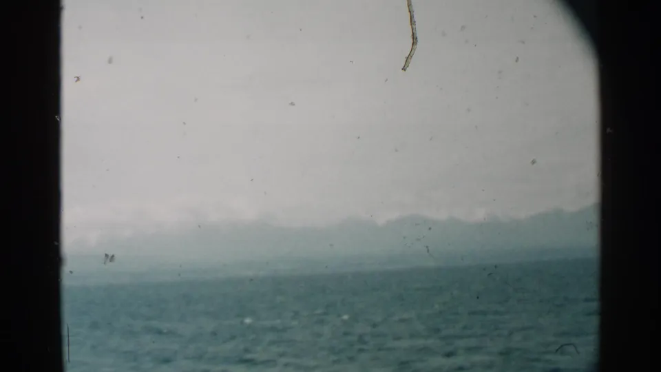 1958 Pearl Harbor view across textured water toward a hazy Hawaiian shoreline, divided by dark porthole framing.