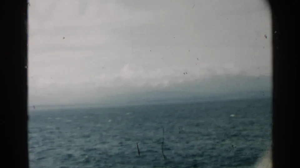 Pearl Harbor 1958 home-movie view of rough blue-green water and a cloud-wrapped distant shoreline through dark framing.