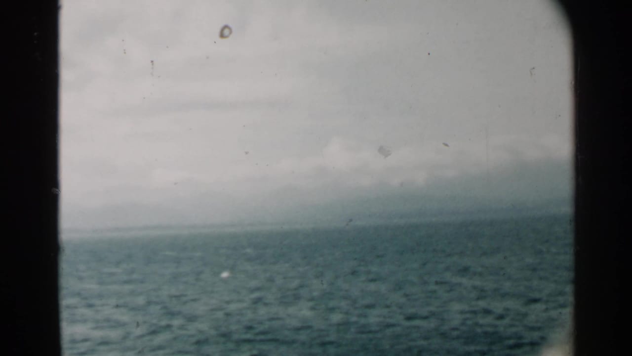 1958 Pearl Harbor home-movie view of calm blue water and distant land through a dark window or porthole edge.