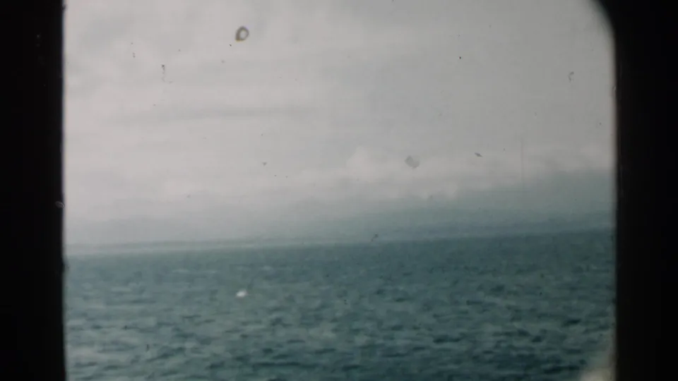 1958 Pearl Harbor home-movie view of calm blue water and distant land through a dark window or porthole edge.