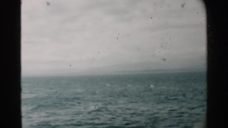 Vintage 8mm view of ocean water near Pearl Harbor, with muted color, soft horizon, and a dark vessel window divider.