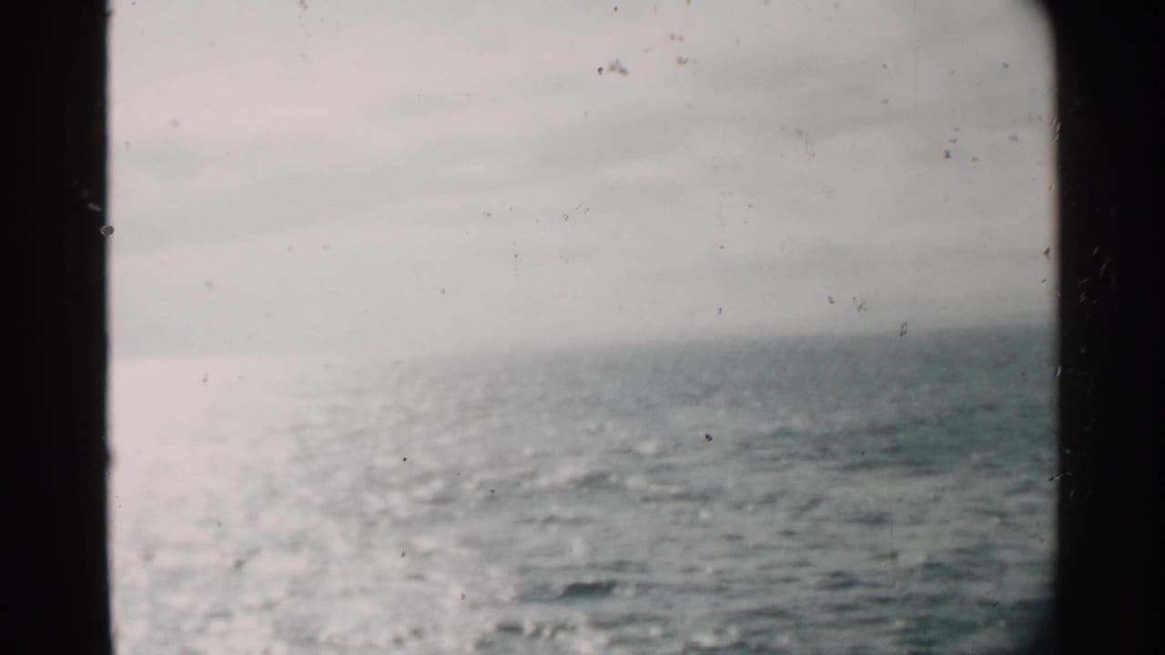 Hazy ocean view from a moving vessel near Pearl Harbor, with bright water and dark film or window framing.