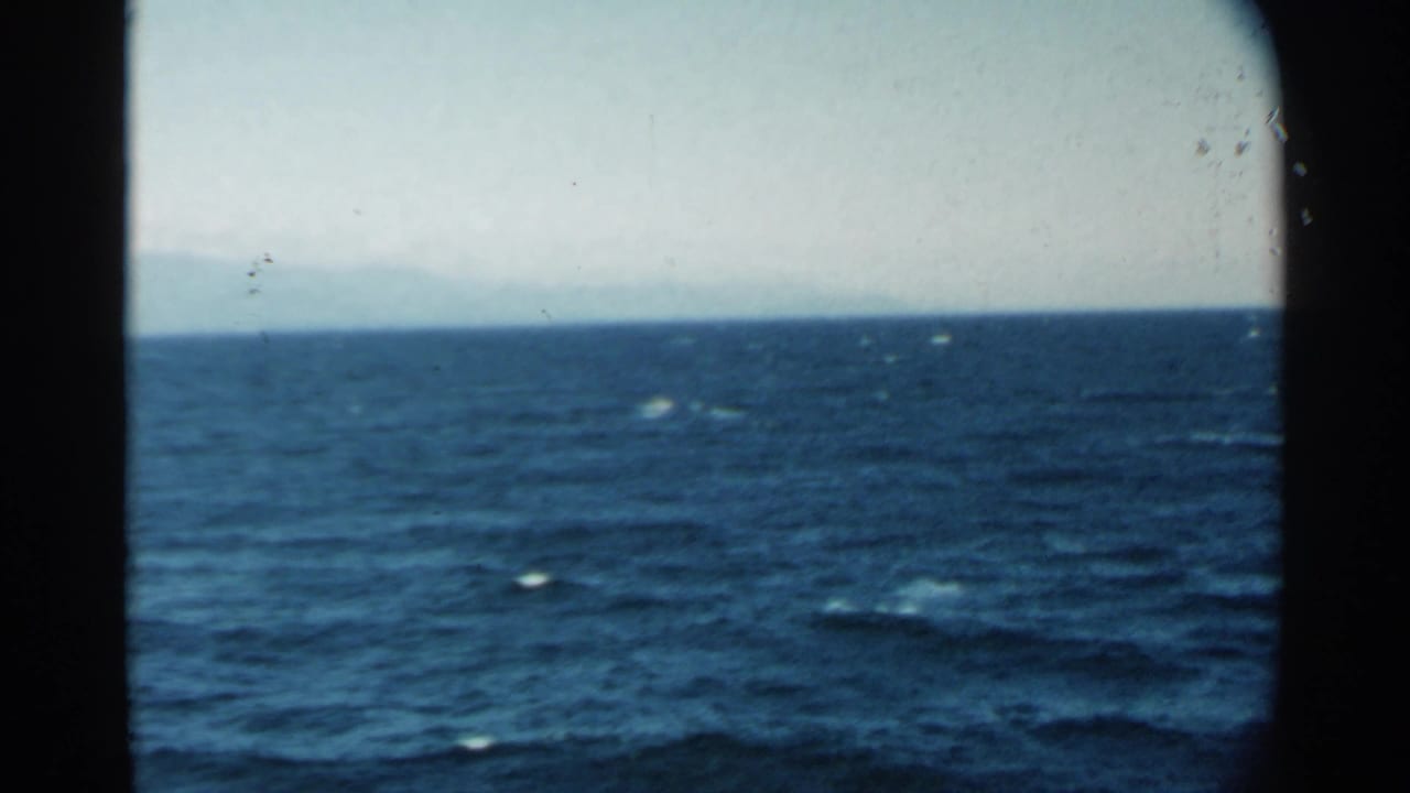 1958 8mm Pearl Harbor-area view of deep blue ocean, pale sky, and faint land seen from a moving vessel.