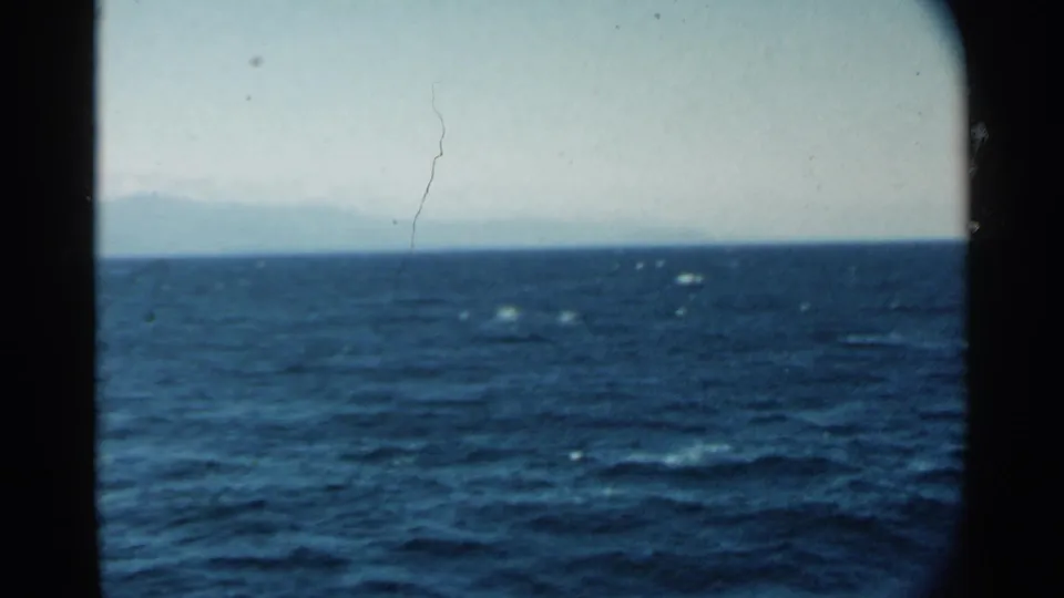 1958 Hawaii vessel-view footage shows open ocean, faint shoreline on the horizon, and visible 8mm film grain and dust.