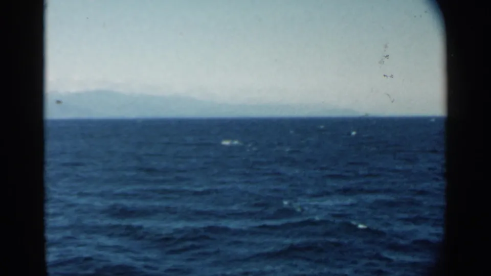 Pearl Harbor-area 8mm frame from 1958 showing blue water, whitecaps, and a hazy landform across the horizon.