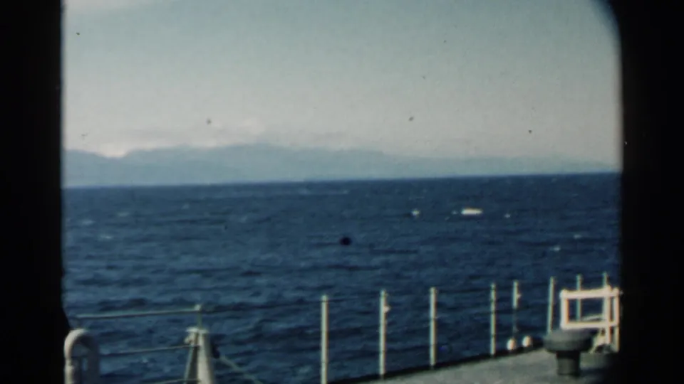 1958 Hawaii ship deck view showing railings at the lower edge, open water, and a distant shoreline under a pale sky.