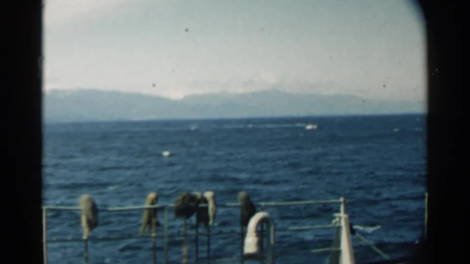 A moving-boat view in Pearl Harbor shows choppy blue water, a soft mountain horizon, and rail-mounted gear in the foreground.