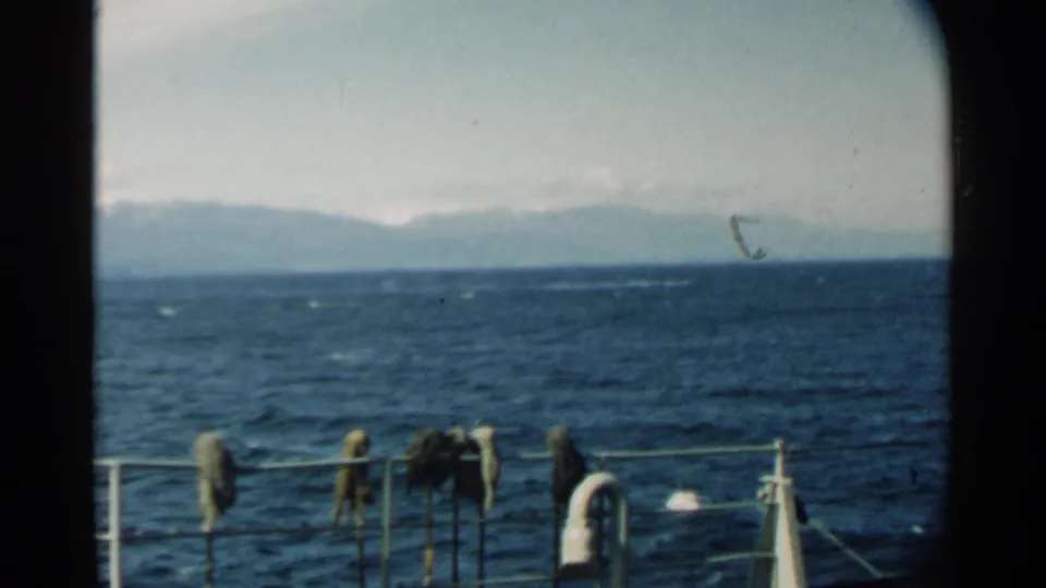 Final frame of a 1958 Pearl Harbor boat view, with dark blue water, hazy mountains, railings, and hanging deck items visible.