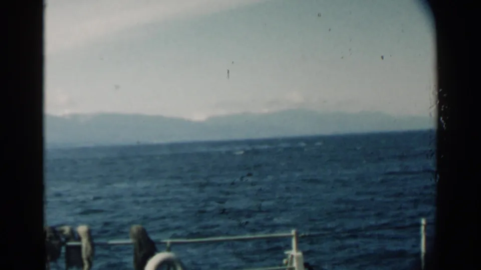 Pearl Harbor 1958 8mm frame showing a low mountain ridge across dark water, with boat railings and circular life-preserver forms along the lower edge.