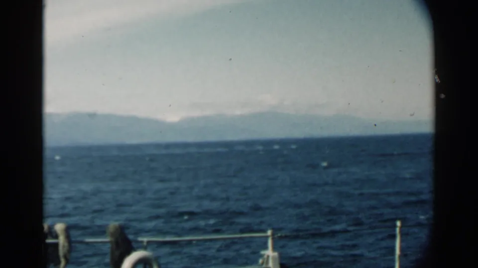 1958 Pearl Harbor-area 8mm frame showing dark ocean, ship railing, a partial life preserver, and hazy mountains on the horizon.