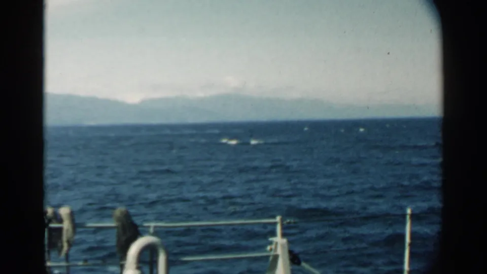 8mm home-movie frame from a Pearl Harbor-area boat ride, showing open water, distant mountains, deck rail, and a partial life preserver.