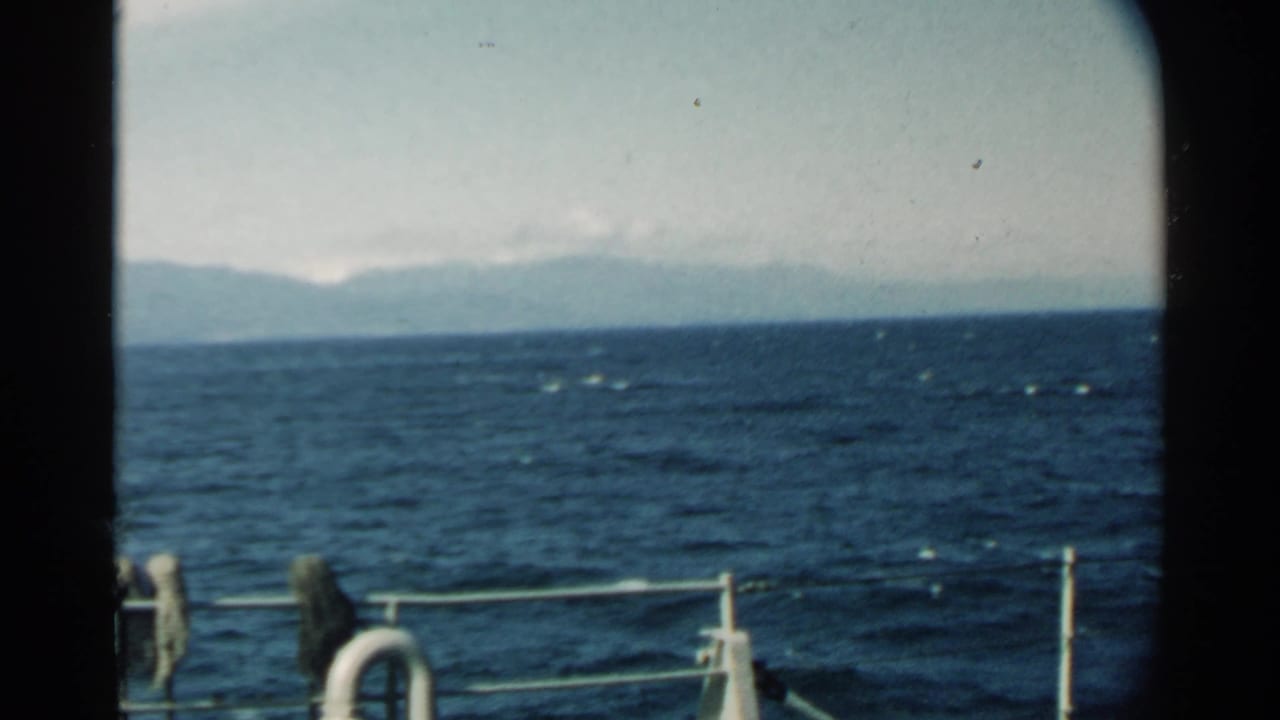 Boat passenger view near Pearl Harbor in 1958, with rolling blue water, white railings, and a hazy mountain horizon.