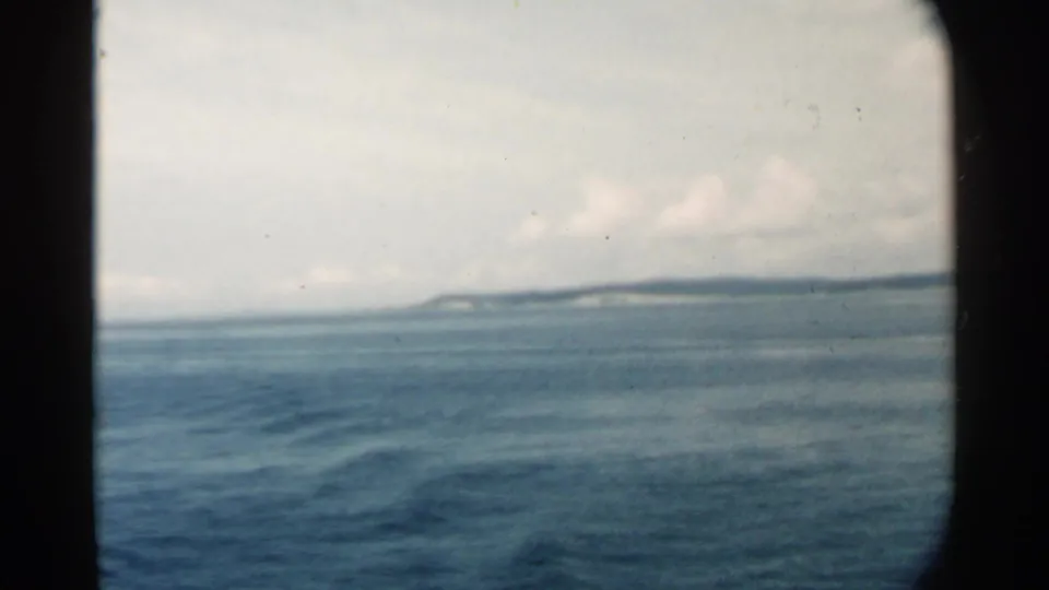 1958 8mm coastal view near Pearl Harbor, showing open water, a faint shoreline, and soft cloud cover on the horizon.