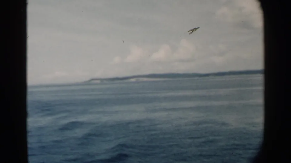 1958 8mm view near Pearl Harbor with blue-gray water, distant shoreline, clouded sky, and visible film or debris mark overhead.