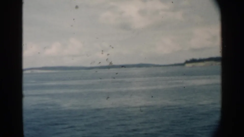 Pearl Harbor-area 8mm frame with open water, a low island horizon, cloudy sky, and dark central vessel-window framing.