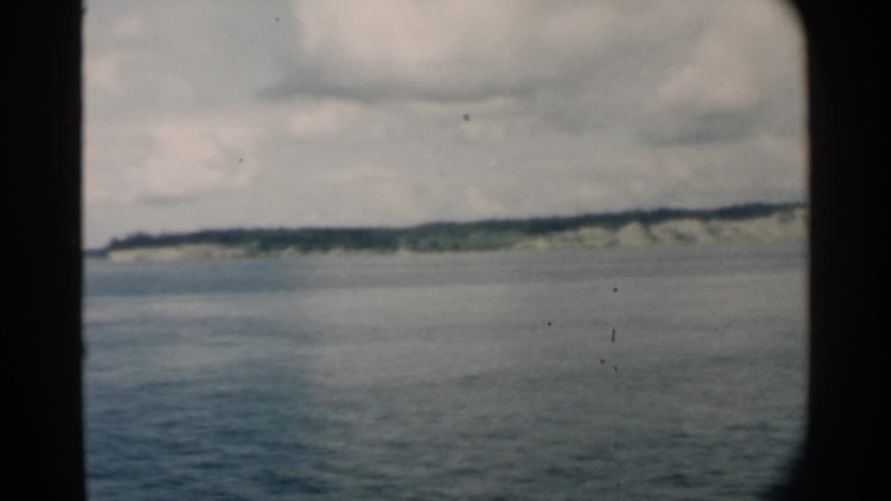 Calm water with a distant low island and pale cliffs beneath a cloudy sky.
