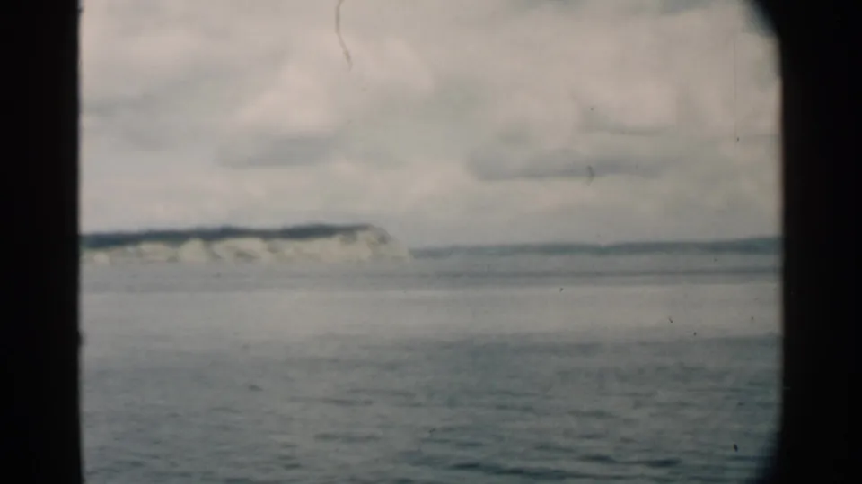 1958 8mm frame from Pearl Harbor showing a pale coastal cliff beyond calm water, with dark contact-sheet borders.