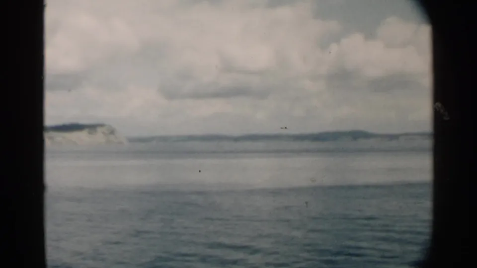 1958 Pearl Harbor coastal view with calm blue-gray water, distant low land, and layered clouds in 8mm texture.