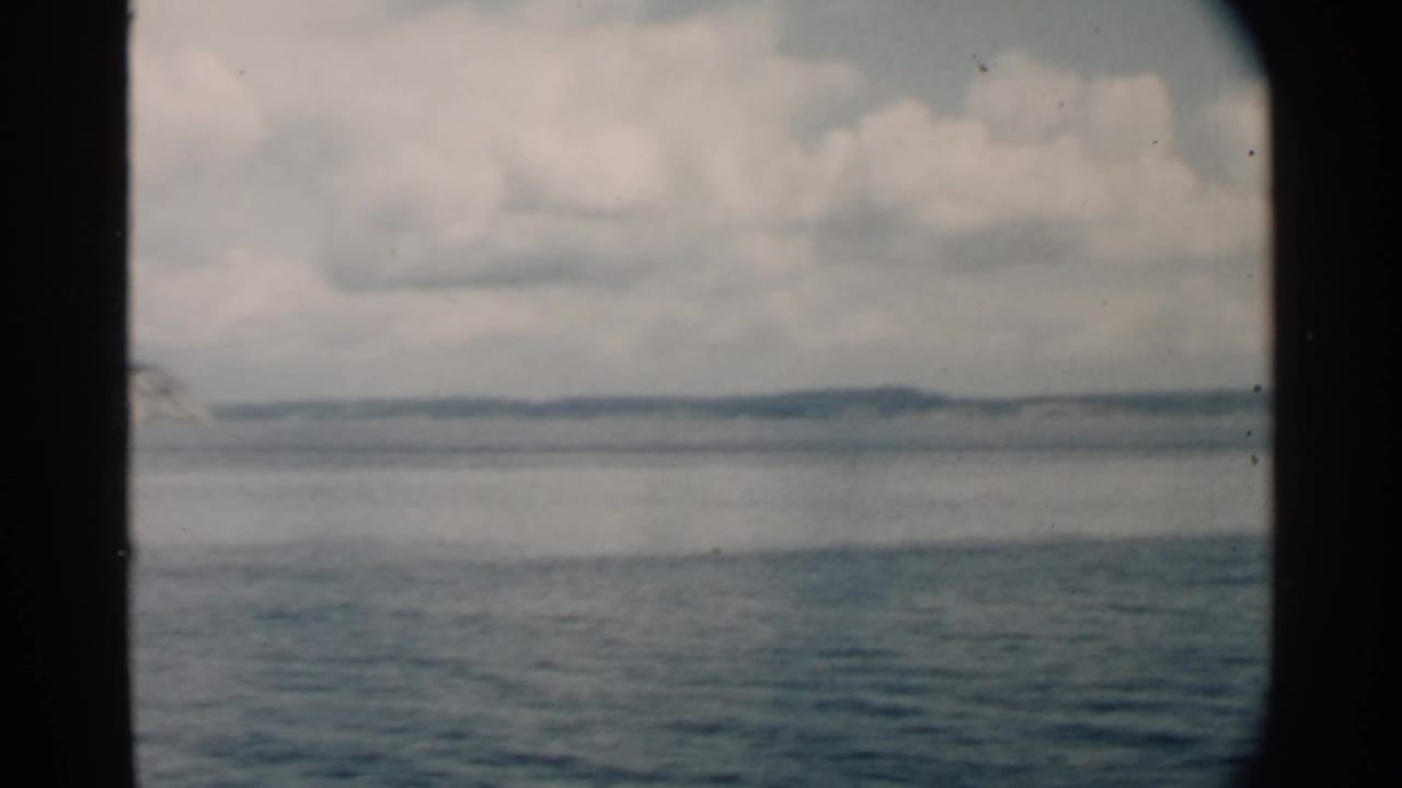 Blue ocean and cloudy sky seen through dark vessel window framing.
