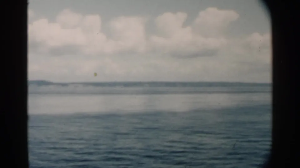 1958 Hawaii home-movie frame showing rippled blue water, a hazy far shore, and large clouds seen from a moving vessel.