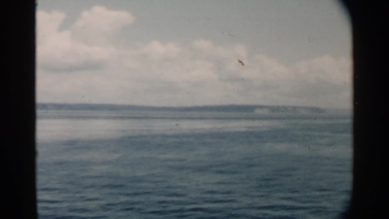 Blue water and distant shoreline seen through a dark boat window frame under cloudy sky.