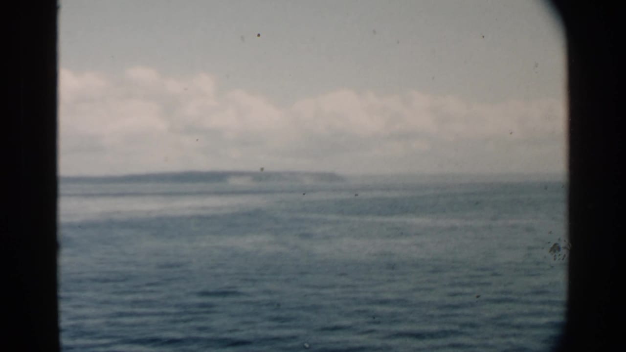 Open water with low land on the horizon and a dark vertical frame edge at left.