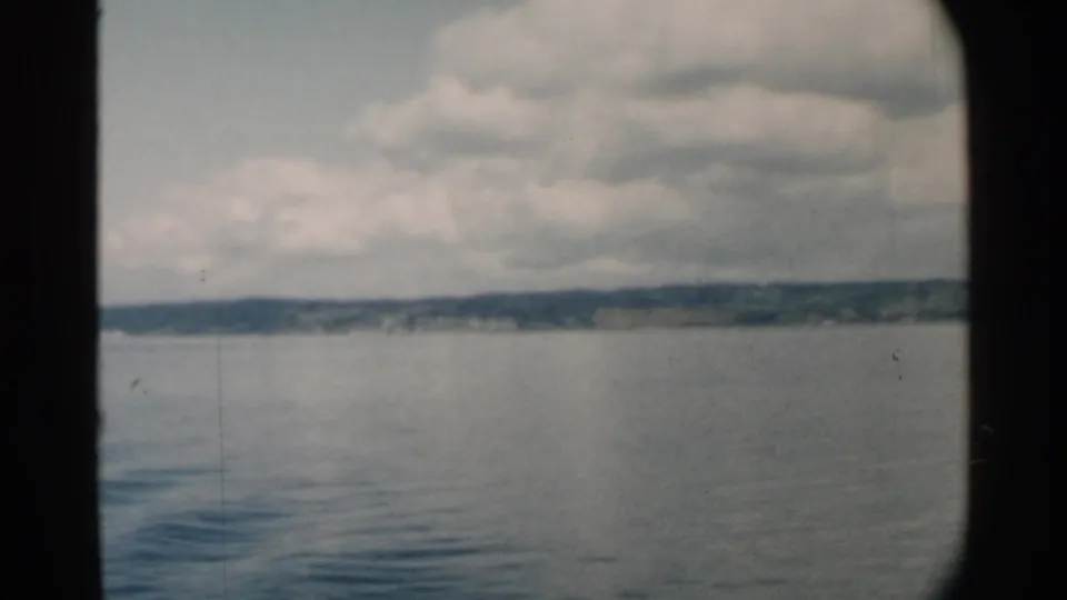 1958 Hawaii harbor view showing smooth water, a distant landmass, and layered clouds, partially bordered by dark boat-window framing.