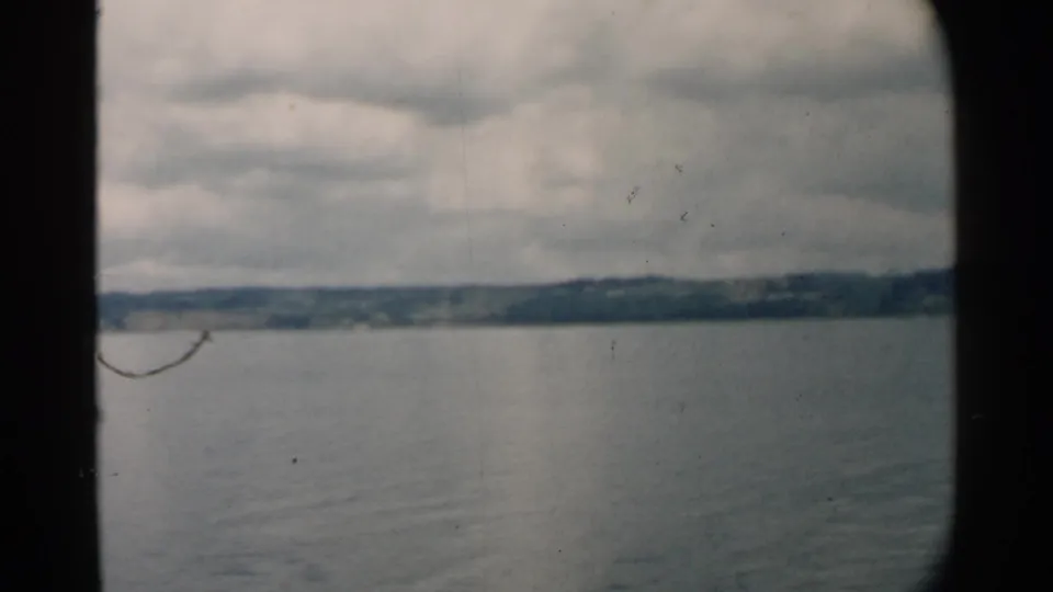 8mm home-movie frame from Pearl Harbor showing gray-blue water, low land across the horizon, and heavy cloud cover.
