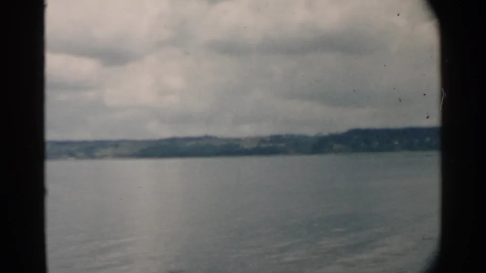 1958 Pearl Harbor 8mm frame with a tree-lined shoreline beyond smooth water and a low, overcast sky.