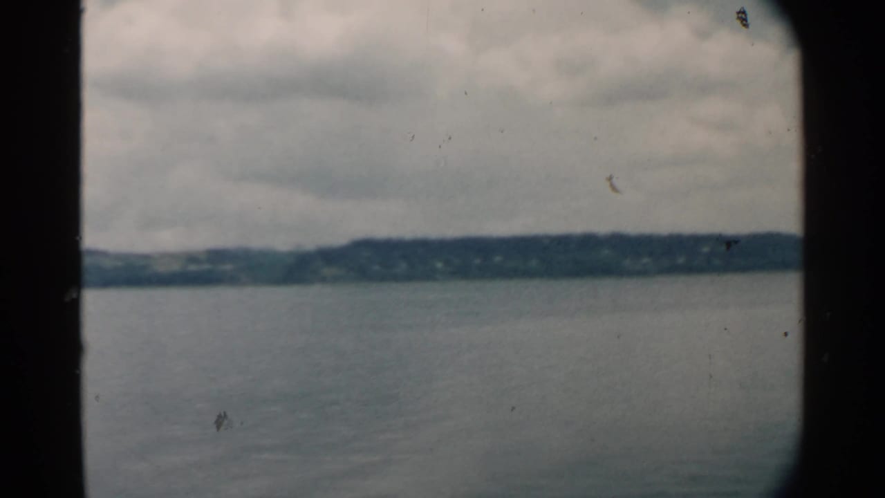 1958 Hawaii harbor view with muted water, low distant land, cloud cover, and dark edge framing from the vessel or film gate.