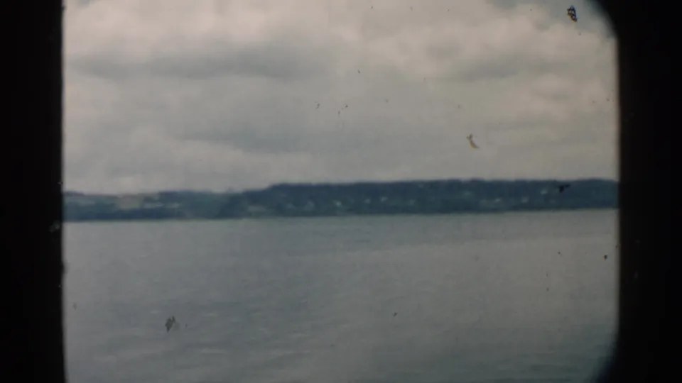 1958 Hawaii harbor view with muted water, low distant land, cloud cover, and dark edge framing from the vessel or film gate.