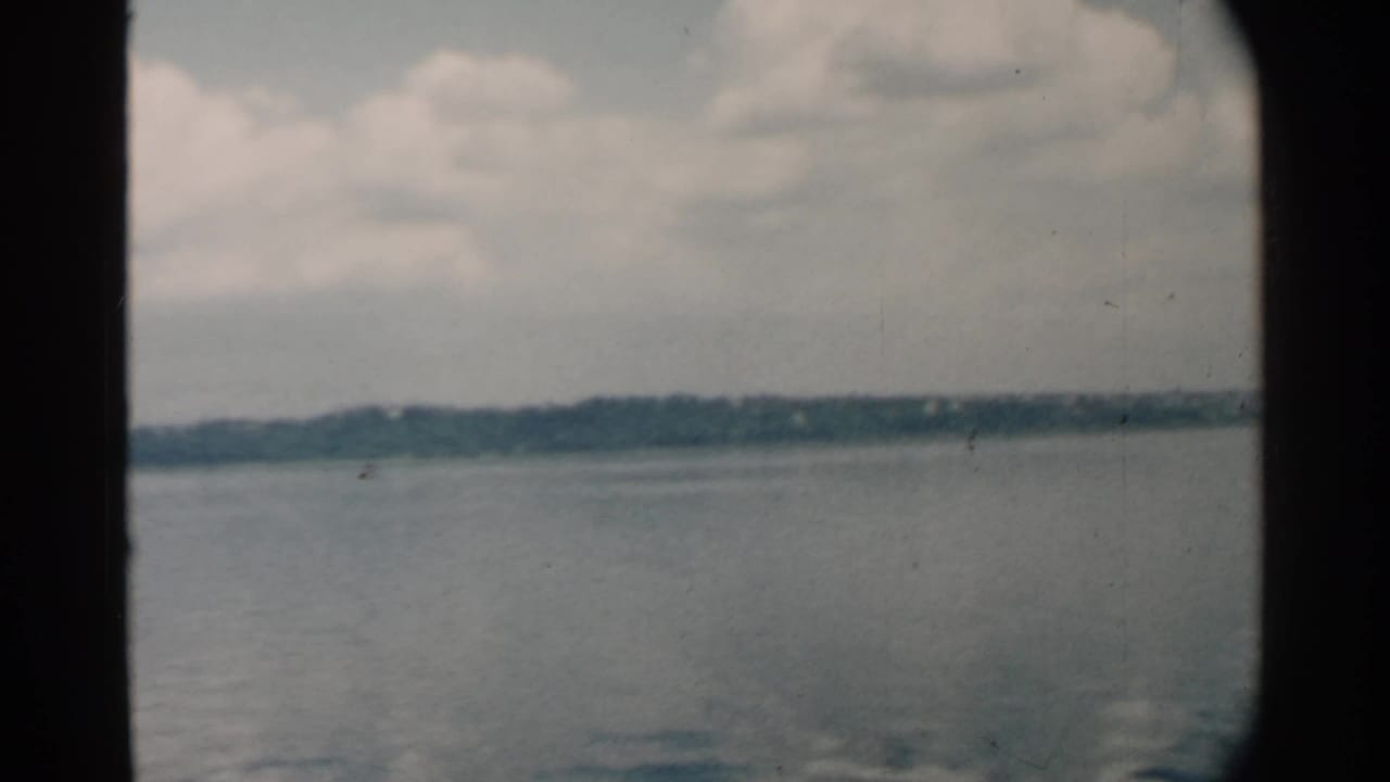Calm water and distant shoreline seen through dark window edges under a cloudy sky.