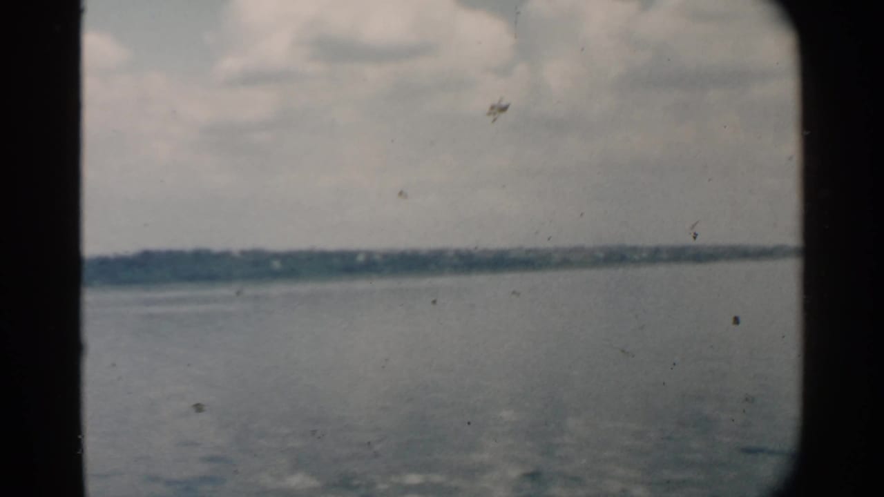 Pearl Harbor water and low distant land appear through a dark framed opening in this 1958 8mm travel shot.