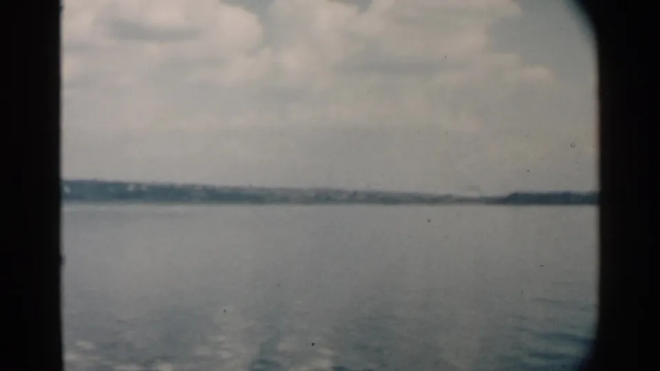 A soft 8mm view of Pearl Harbor water, distant land, and pale clouds, framed by the edge of a vessel window.