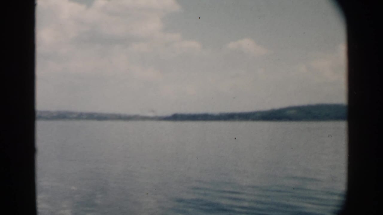 Calm water and distant tree-lined shoreline seen through a dark boat-window frame.