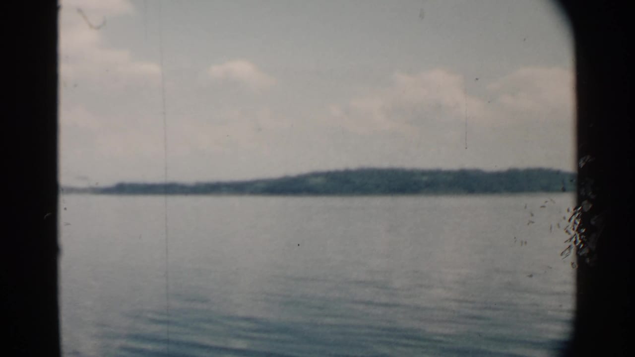 1958 Pearl Harbor frame with calm water, a low tree-covered horizon, pale clouds, and boat-window framing.