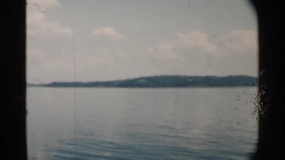 1958 Pearl Harbor frame with calm water, a low tree-covered horizon, pale clouds, and boat-window framing.