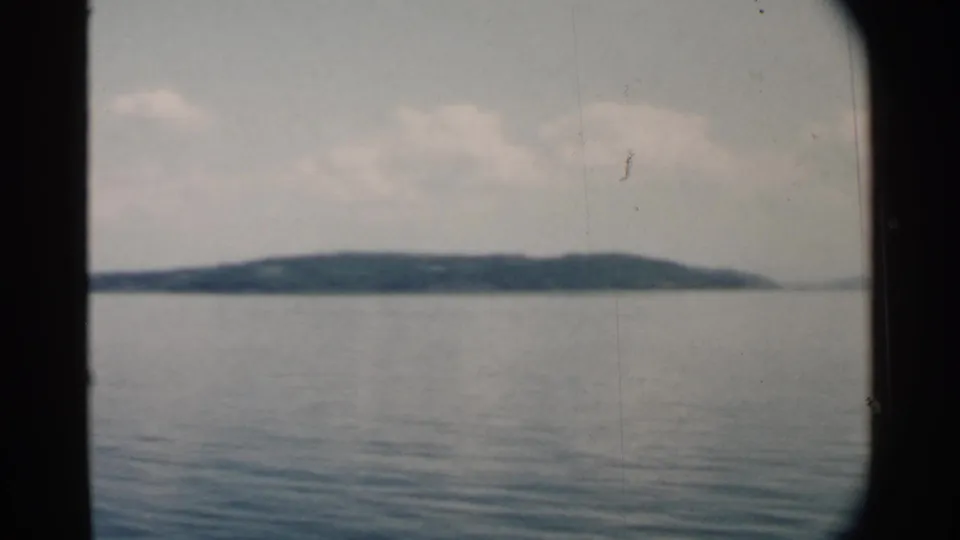 1958 Pearl Harbor home-movie frame showing a low shoreline beyond still water, with soft film grain and window-edge framing.