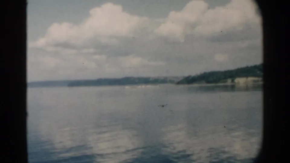 1958 Pearl Harbor view with a green shoreline, light cliff face, calm water, and white clouds framed by dark film edges.
