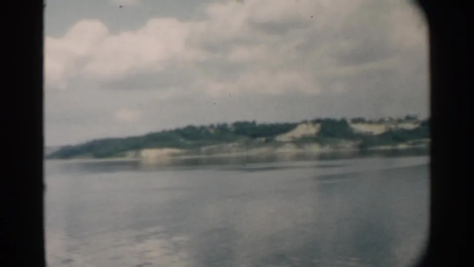 1958 Pearl Harbor coastal view with rippled water, distant green land, pale cliff faces, and large soft clouds.