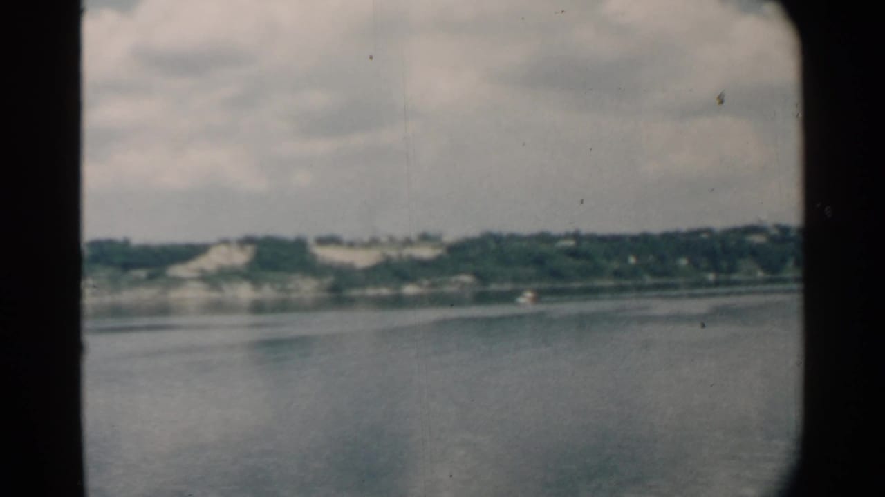 Distant shoreline and water viewed through dark rounded window framing.